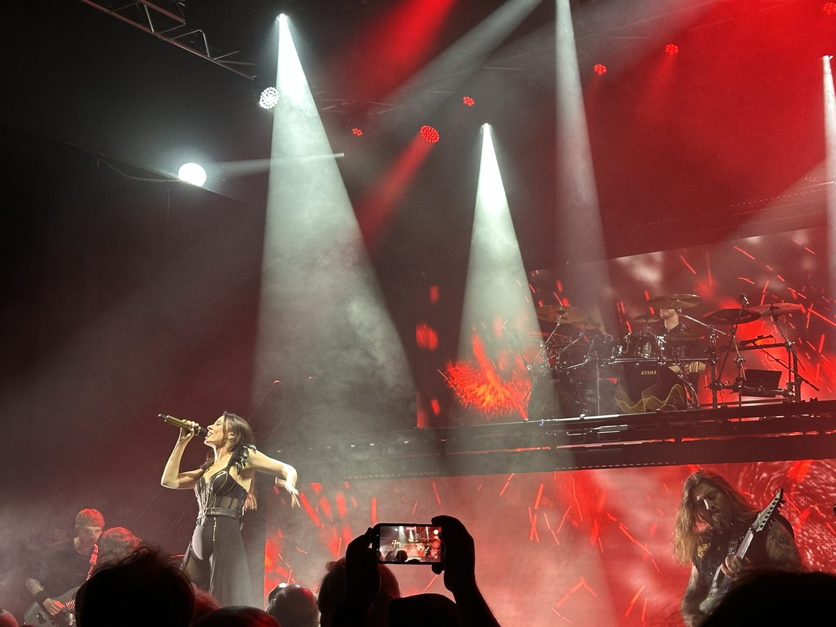 Singer under white spotlights with a raised drum platform and red lighting